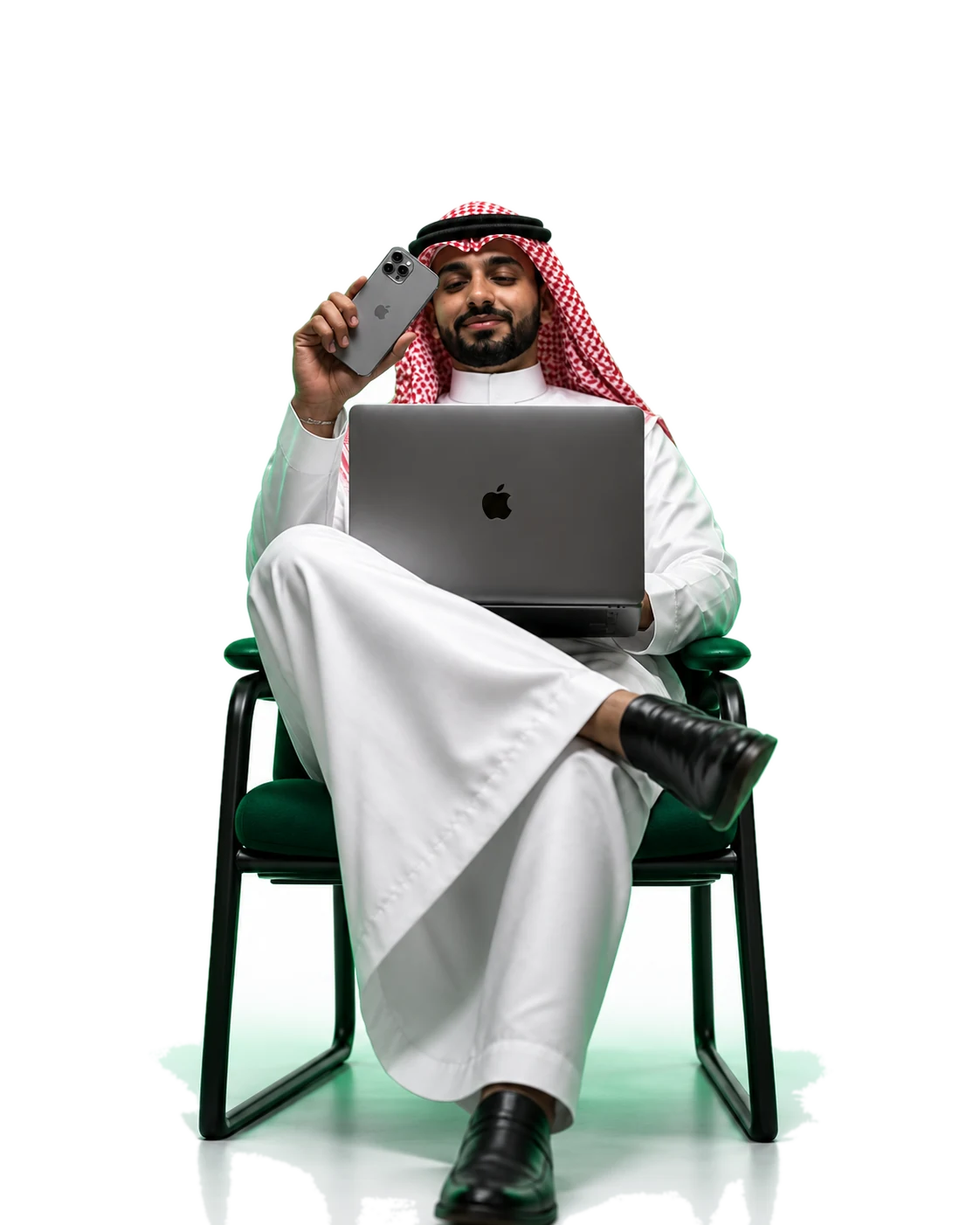 رجل أعمال سعودي يحمل هاتفًا ويعمل على حاسبه